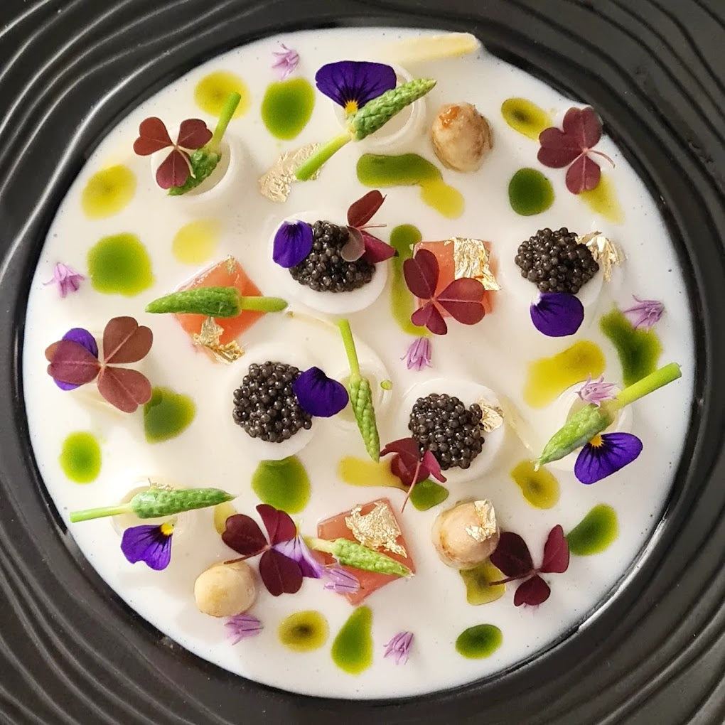 Salle de restaurant lumineuse et élégante, avec un parquet en bois clair et des tables rondes dressées avec des nappes blanches.