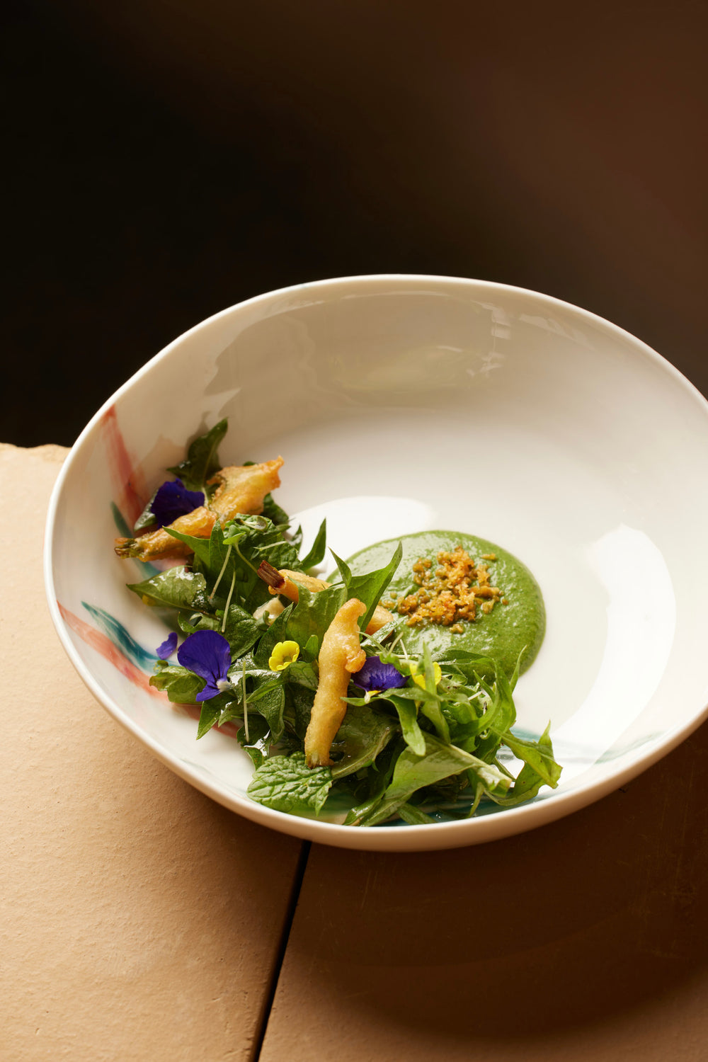 Assiette gastronomique colorée avec des herbes fraîches, fleurs comestibles, et un coulis vert, présentée de manière élégante dans une assiette blanche.