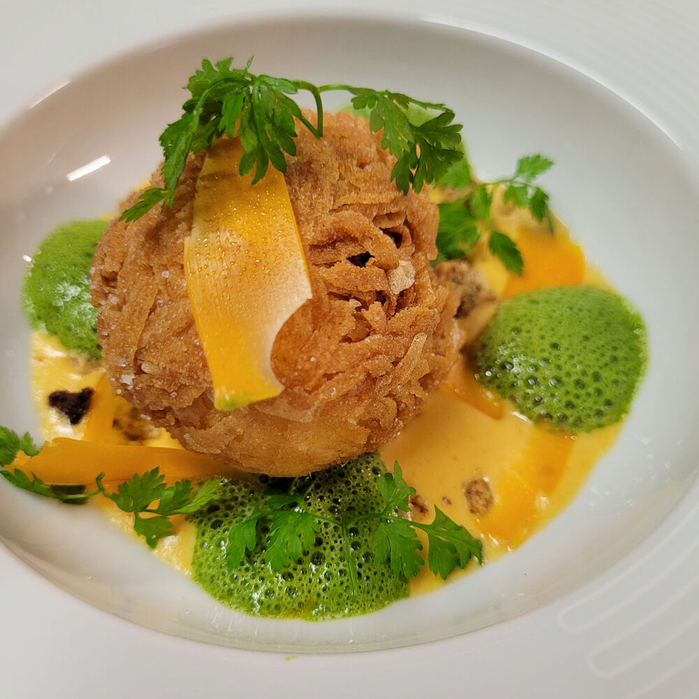 Plat raffiné avec croustillant doré, sauce crémeuse et émulsion verte, décoré de fines herbes.
