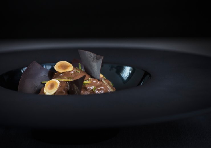 Dessert au chocolat et noisettes dans une assiette noire élégante.