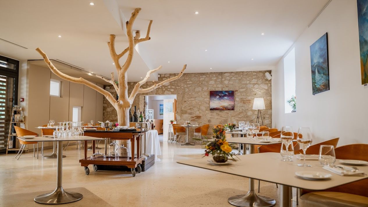 Intérieur d'un restaurant élégant avec des tables dressées, un grand arbre décoratif au centre, des murs en pierre et une ambiance lumineuse et chaleureuse.