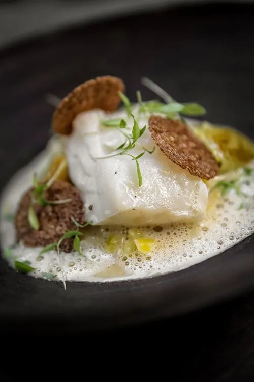 Poisson blanc garni d'herbes et de chips croustillantes dans une sauce mousseuse