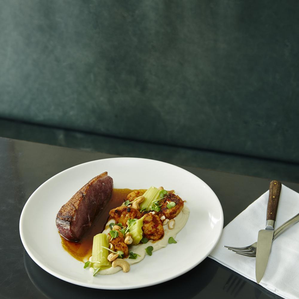 Plat gastronomique avec viande, purée et légumes verts, présenté sur une table moderne.