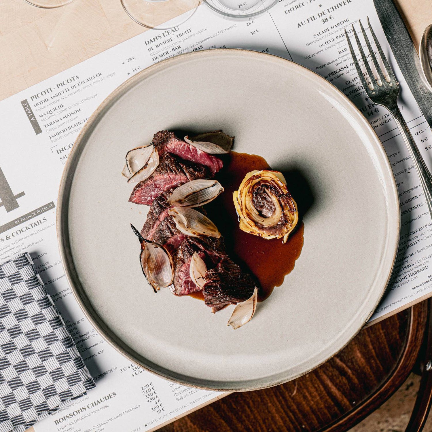 Assiette de viande rouge grillée avec échalotes rôties et roulé de légumes, servie avec une sauce sur un plat élégant.