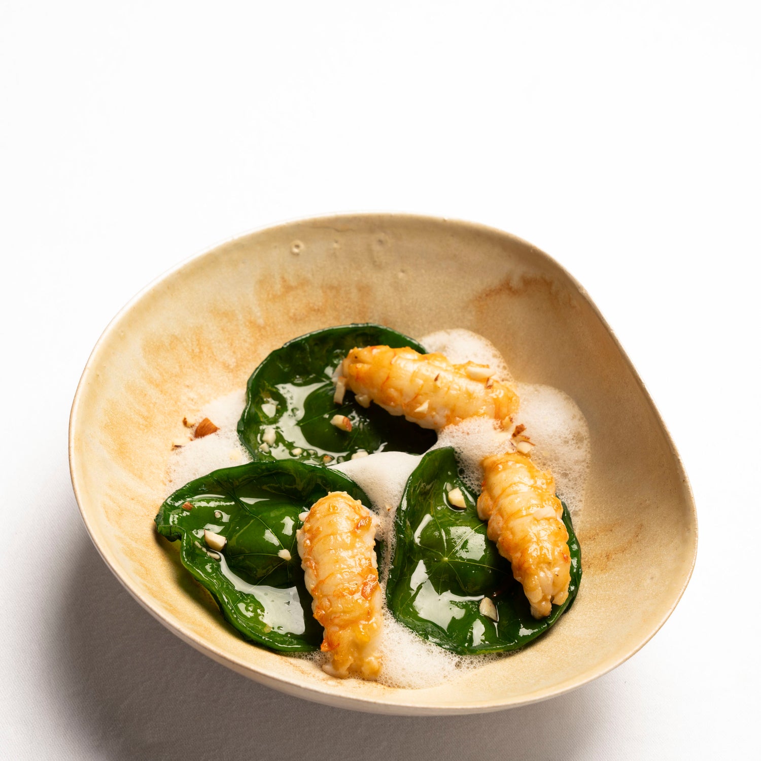 Assiette raffinée composée de crustacés dorés, feuilles vertes et écume légère, dressée dans une céramique artisanale.