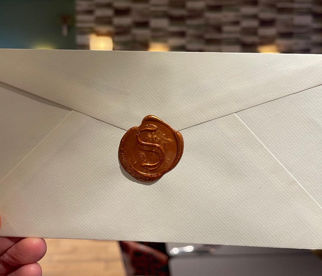 Enveloppe scellée avec un cachet de cire portant un motif en forme de 'S', posée sur un fond flou.