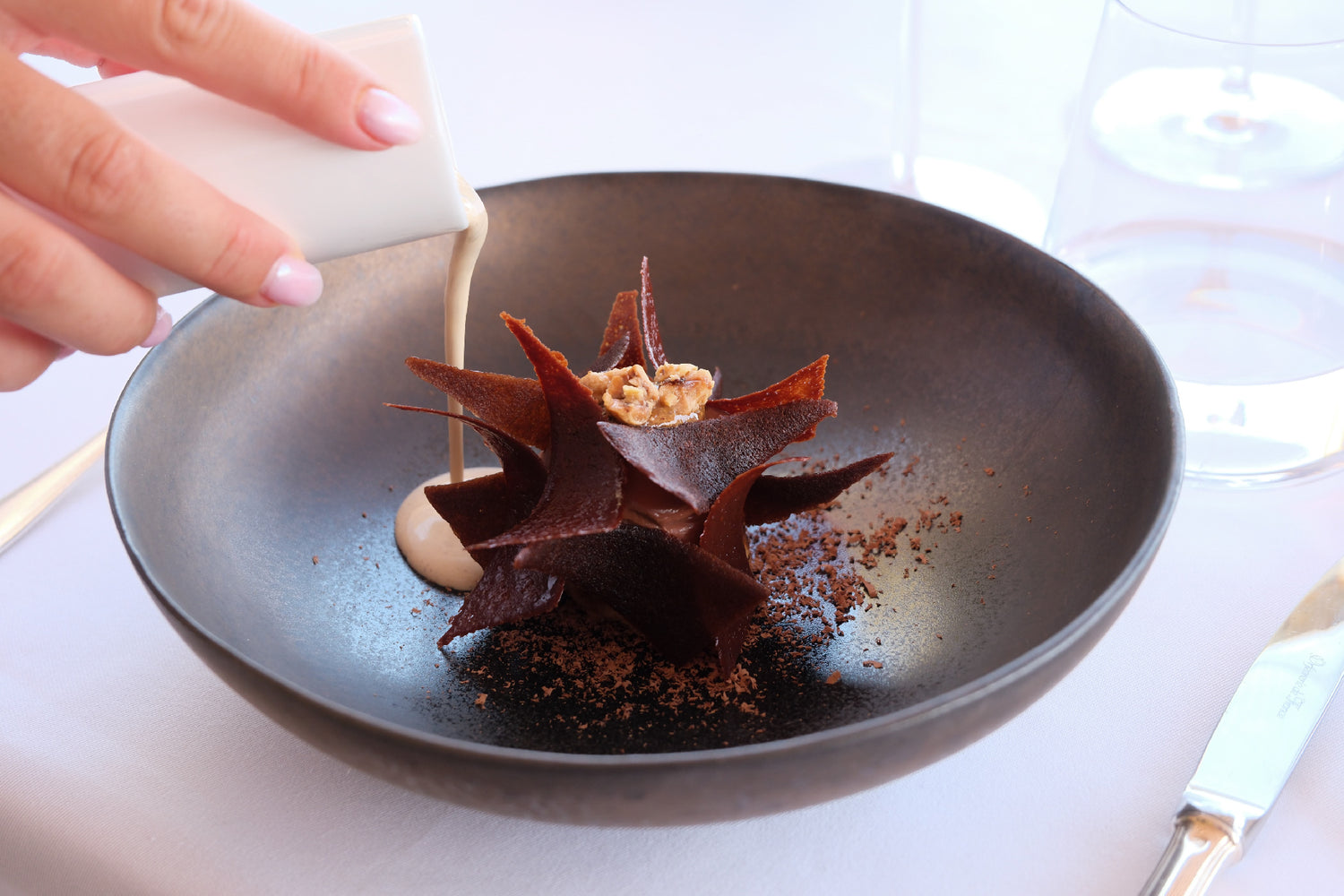 Dessert chocolaté artistique dans un bol noir, avec sauce onctueuse versée à la main, mettant en valeur une présentation raffinée.