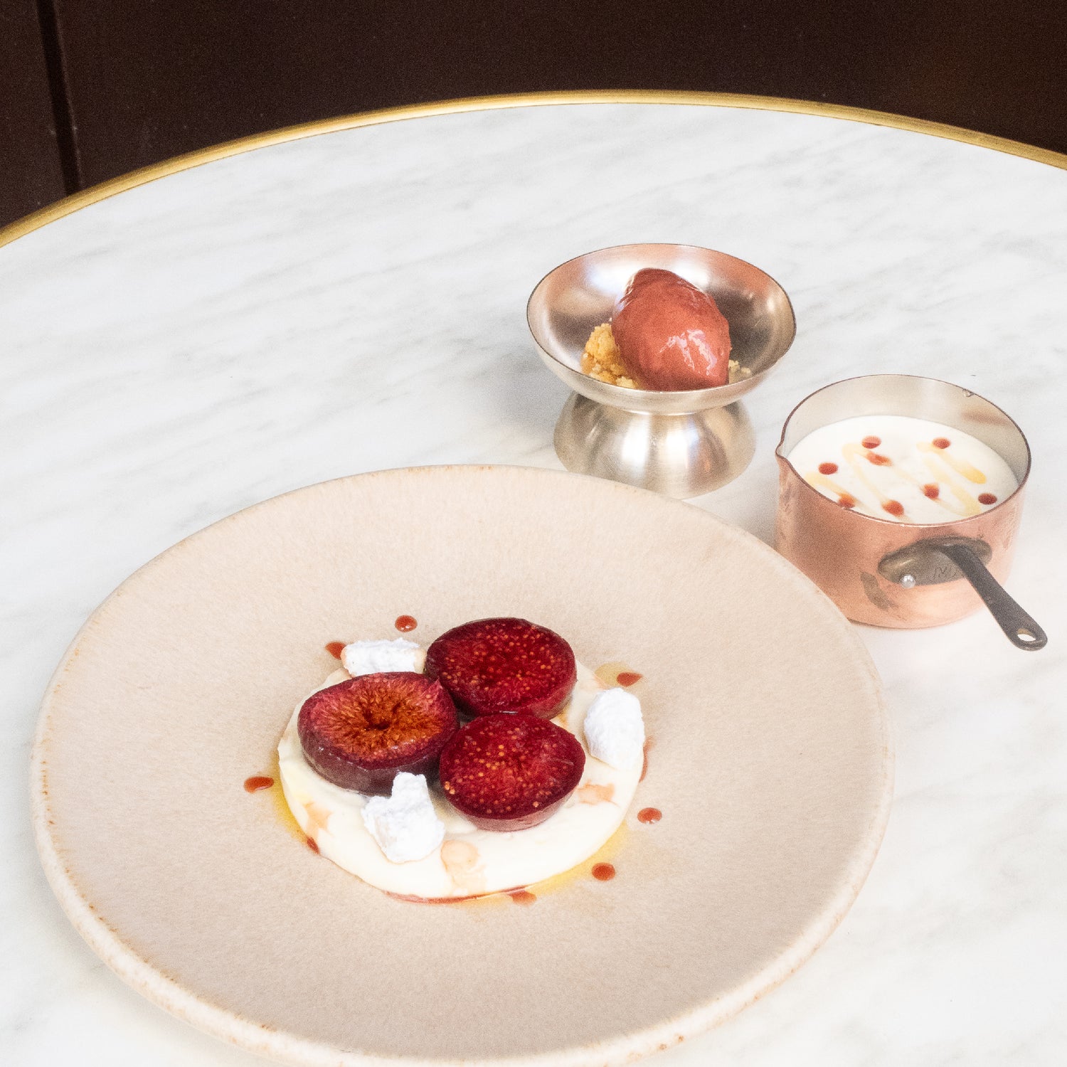 Dessert raffiné à base de figues rôties, crème et glace, joliment présenté sur une table en marbre.