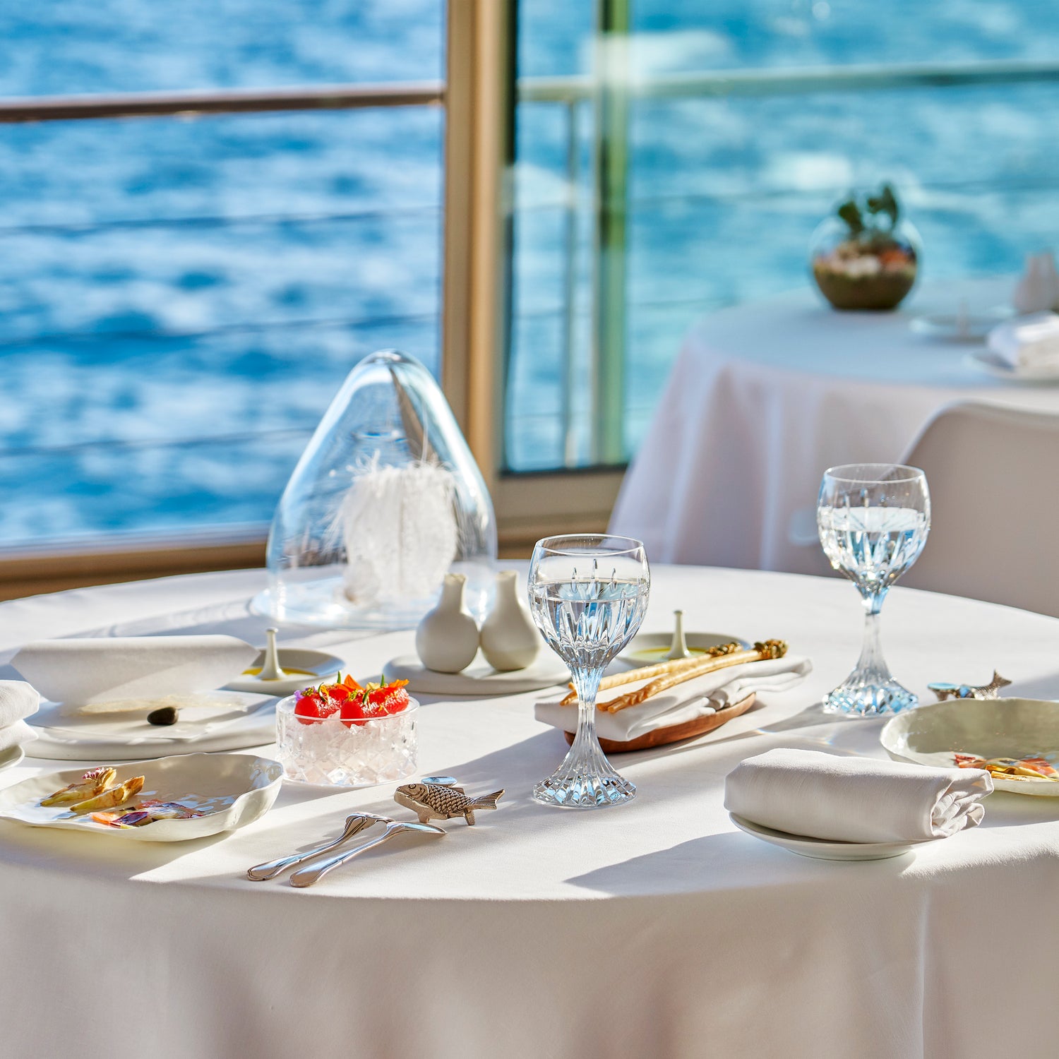 Table élégamment dressée avec vue sur la mer, dans un restaurant gastronomique, ornée de verres en cristal et de plats raffinés, créant une atmosphère de luxe et de sérénité.
