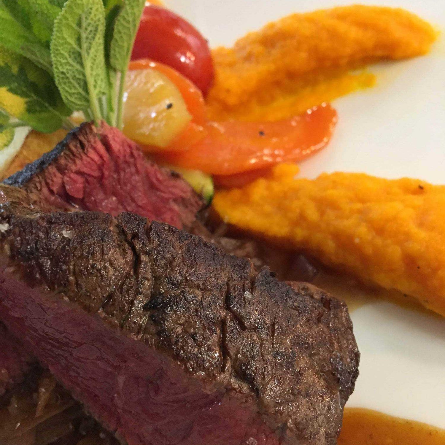 Pièce de viande rouge grillée accompagnée de purée de carottes et légumes colorés, garnie d'herbes fraîches.