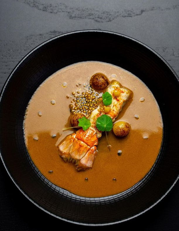 Langoustine immergée à moitié dans une sauce se rapprochant d'une bouillabaisse