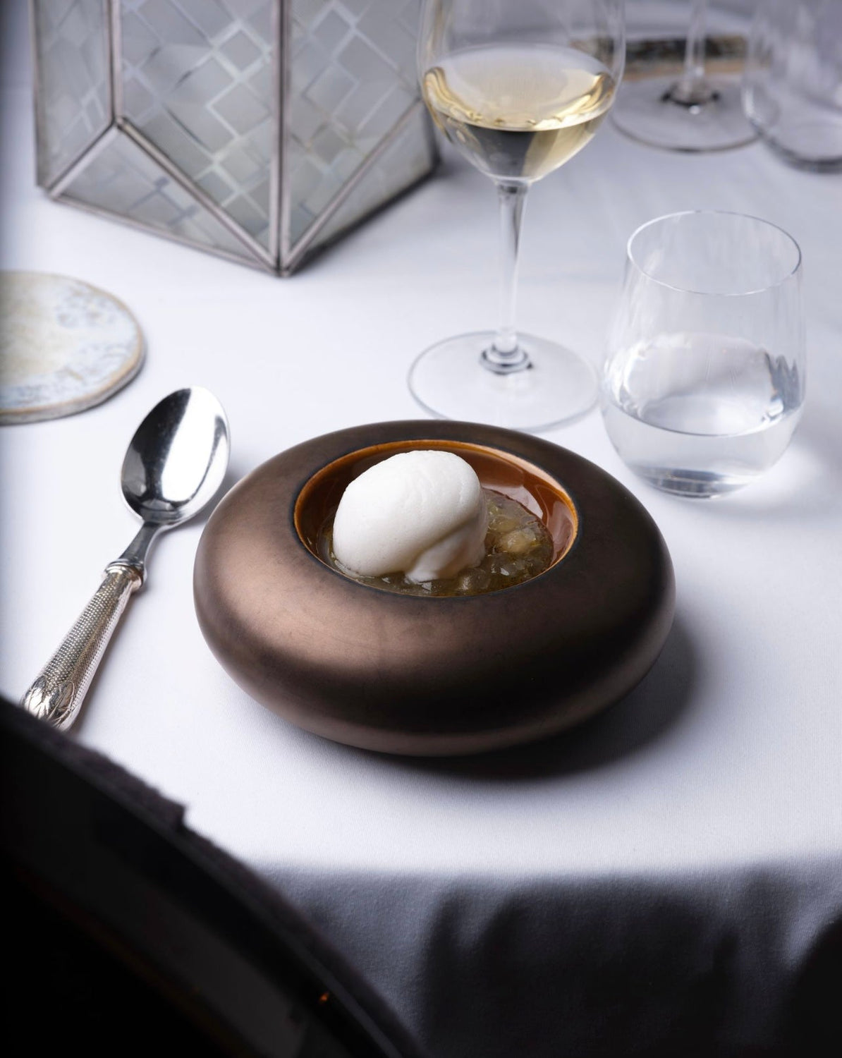 Dessert raffiné avec une boule de glace sur une gelée, servi dans un bol design en bronze, accompagné d'un verre de vin blanc.