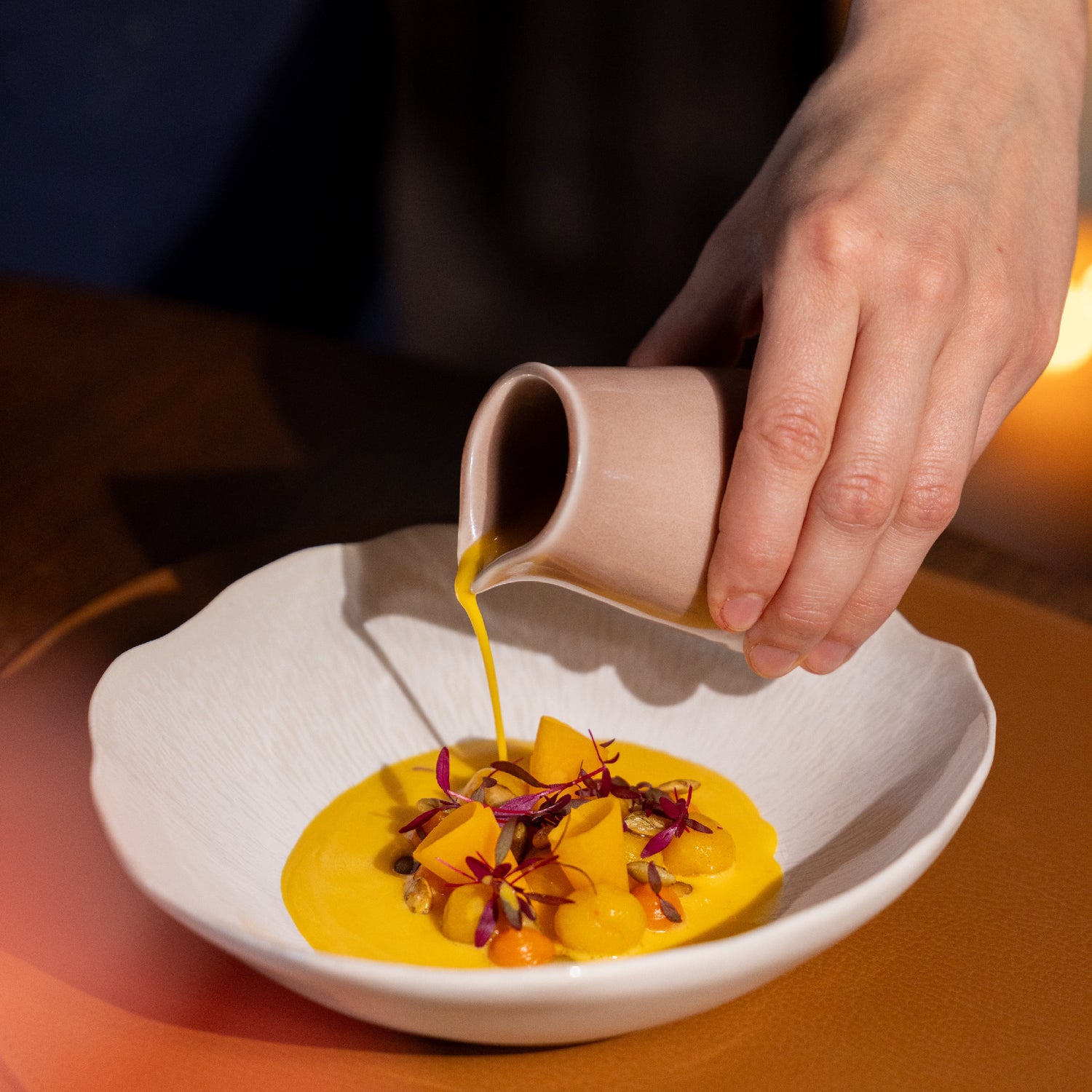 Assiette gastronomique avec un velouté de potiron versé sur une préparation colorée, décorée de fleurs comestibles et de dés de légumes.