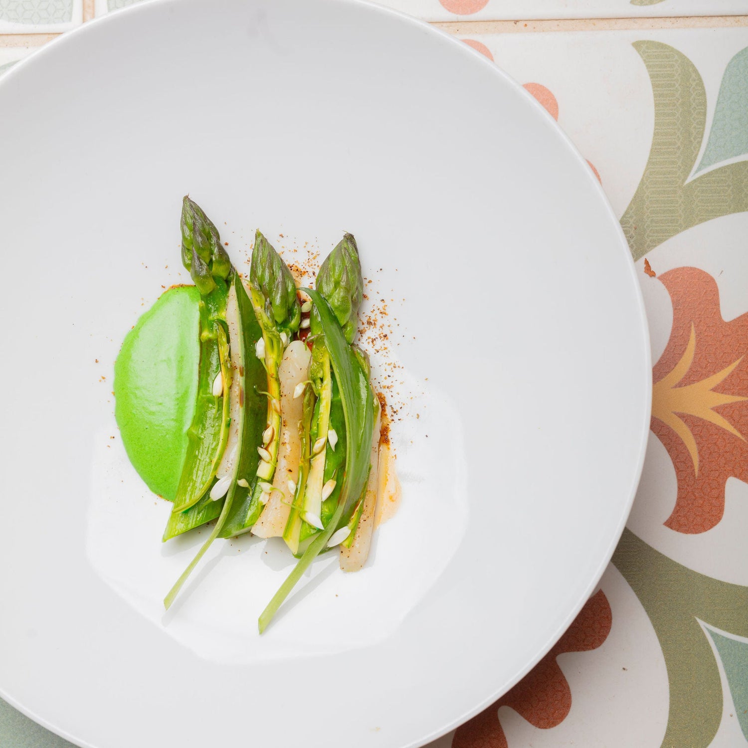 Assiette blanche avec des asperges vertes artistiquement disposées et une sauce verte sur le côté.