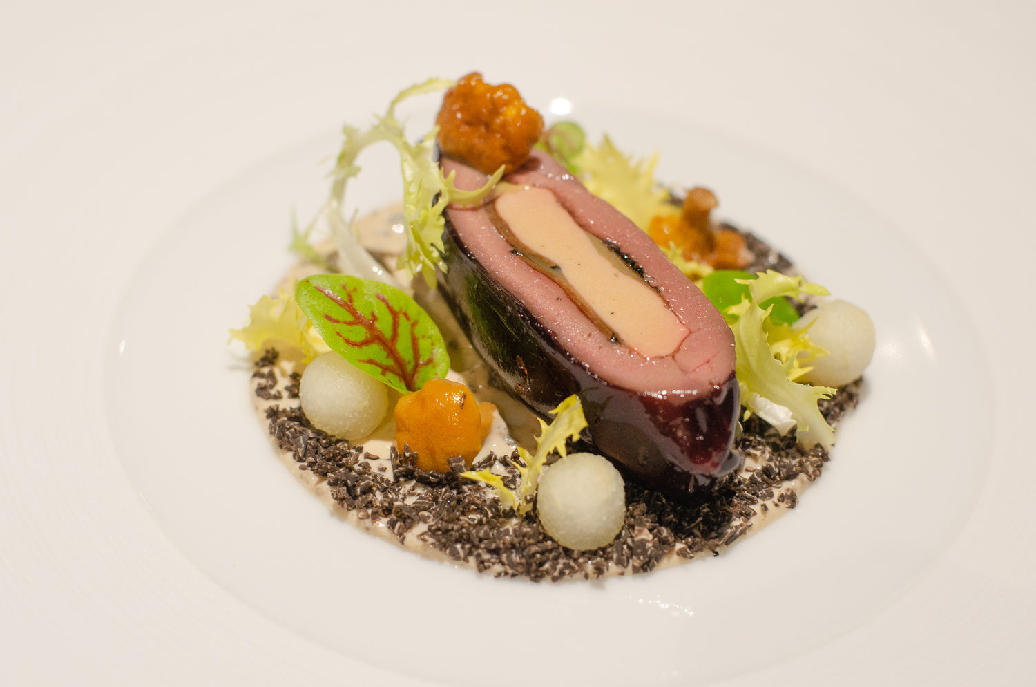 Plat gastronomique composé de pigeon des Costières, foie gras du Gubernat, truffe noire et poire nashi, joliment présenté sur une assiette.