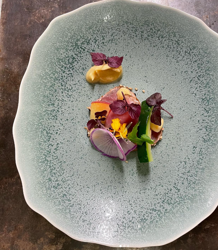 Assiette gastronomique élégante avec une présentation artistique de légumes, herbes et viande, servie sur une assiette texturée verte.