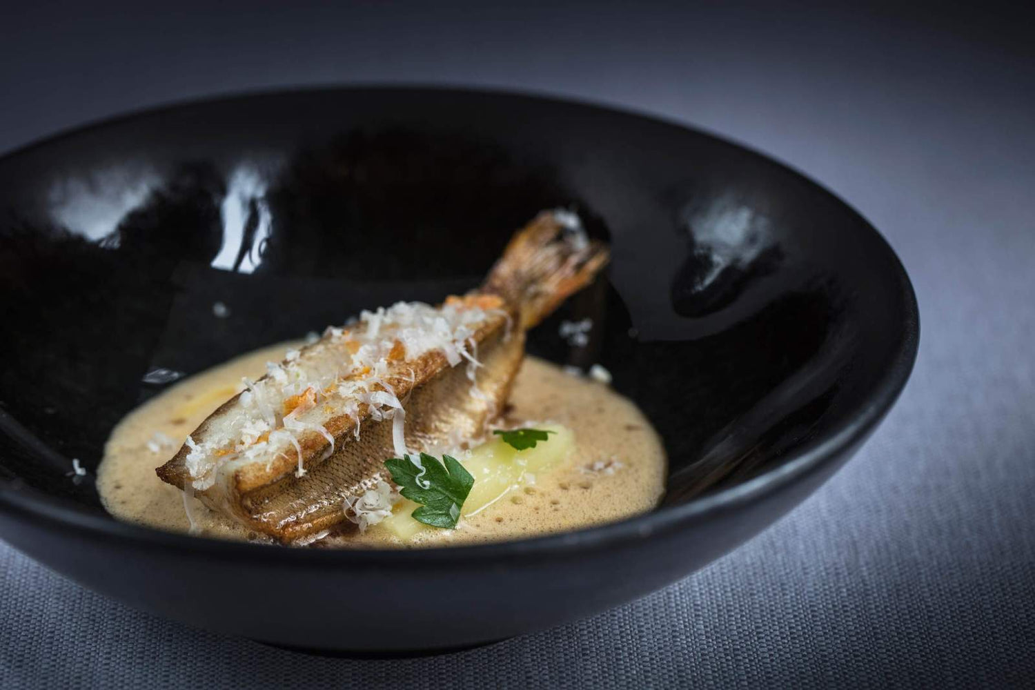 Plat de poisson délicatement présenté dans une assiette noire avec une sauce mousseuse.