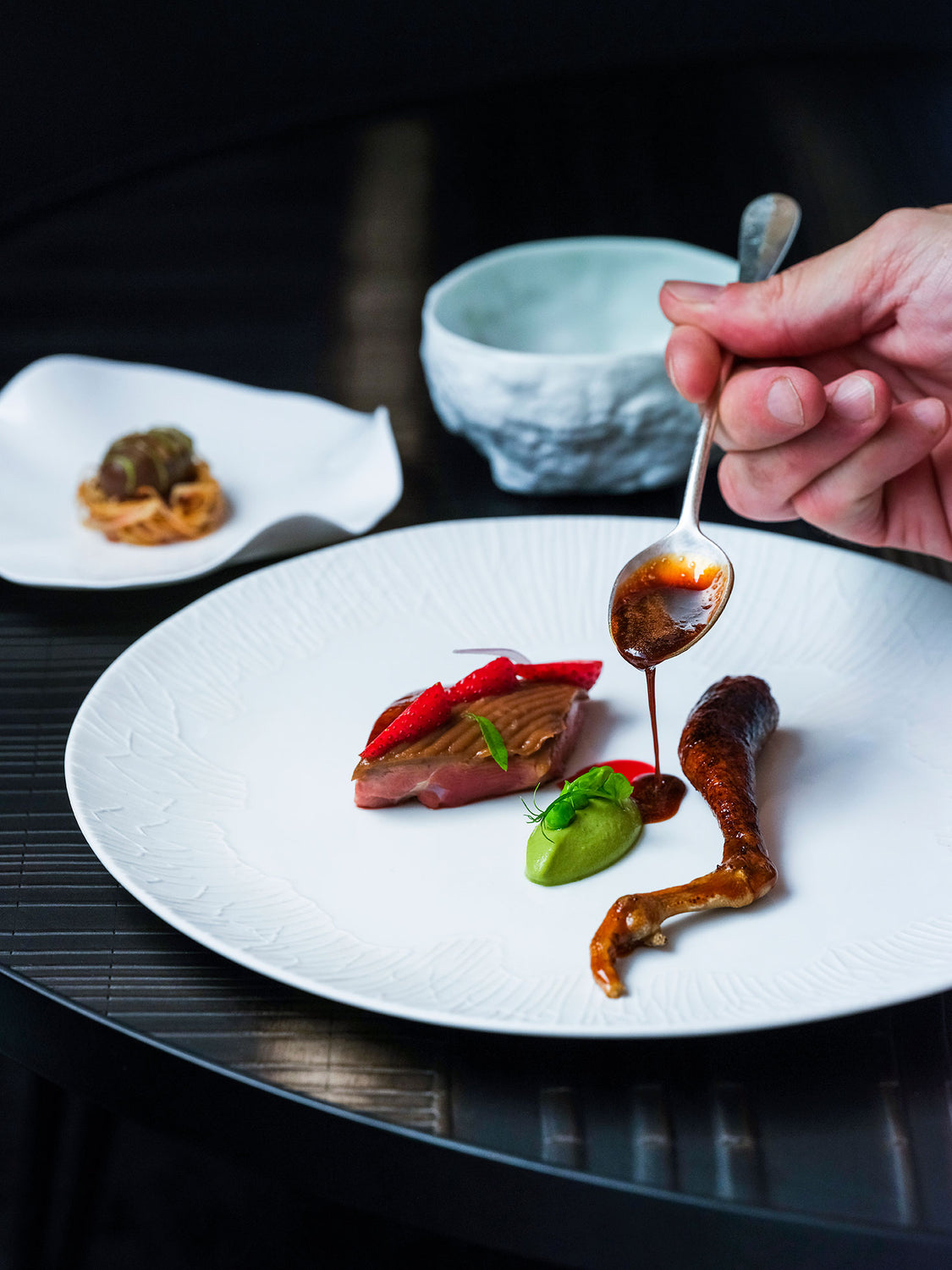 Plat raffiné mettant en scène un pigeon accompagné de fraises, d'une purée verte et d'une sauce ajoutée avec précision par une main de chef.