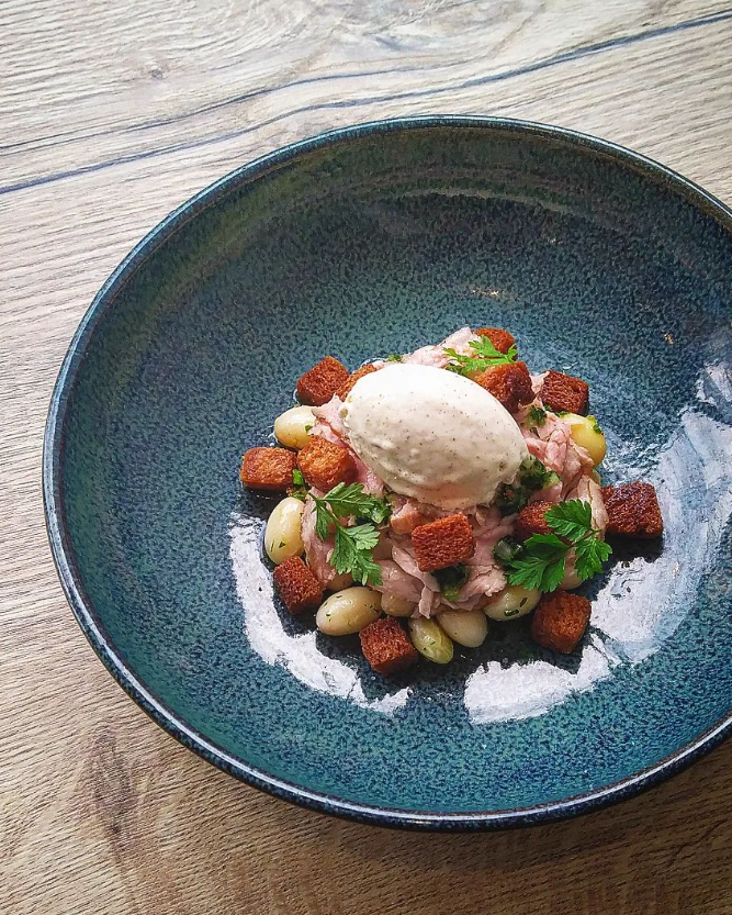 Salade composée de morceaux de viande, croûtons dorés et haricots, surmontée d'une quenelle de crème.