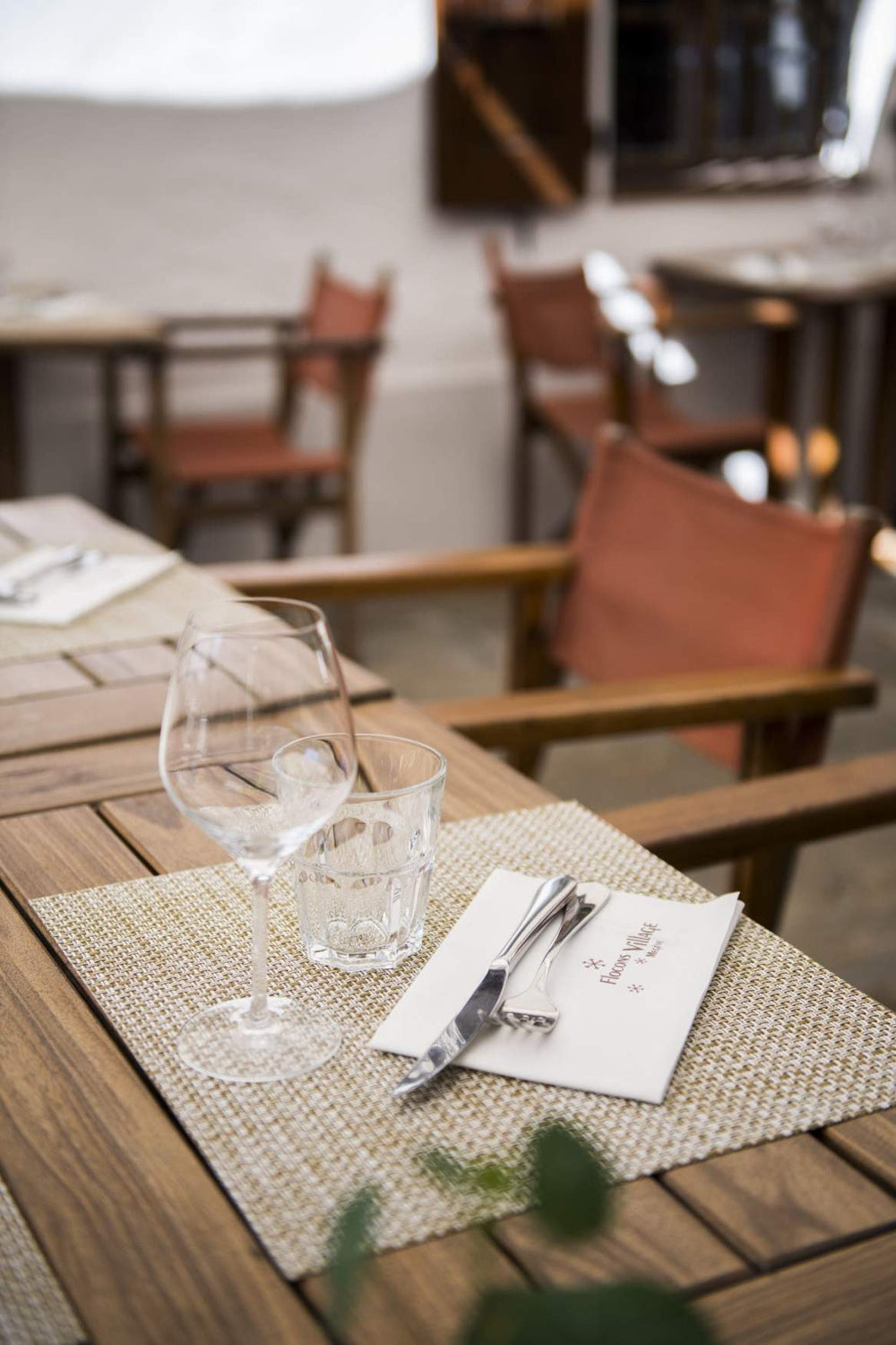 "Table de restaurant en bois avec des chaises en toile, mise en place avec verre à vin, verre à eau, et couverts."