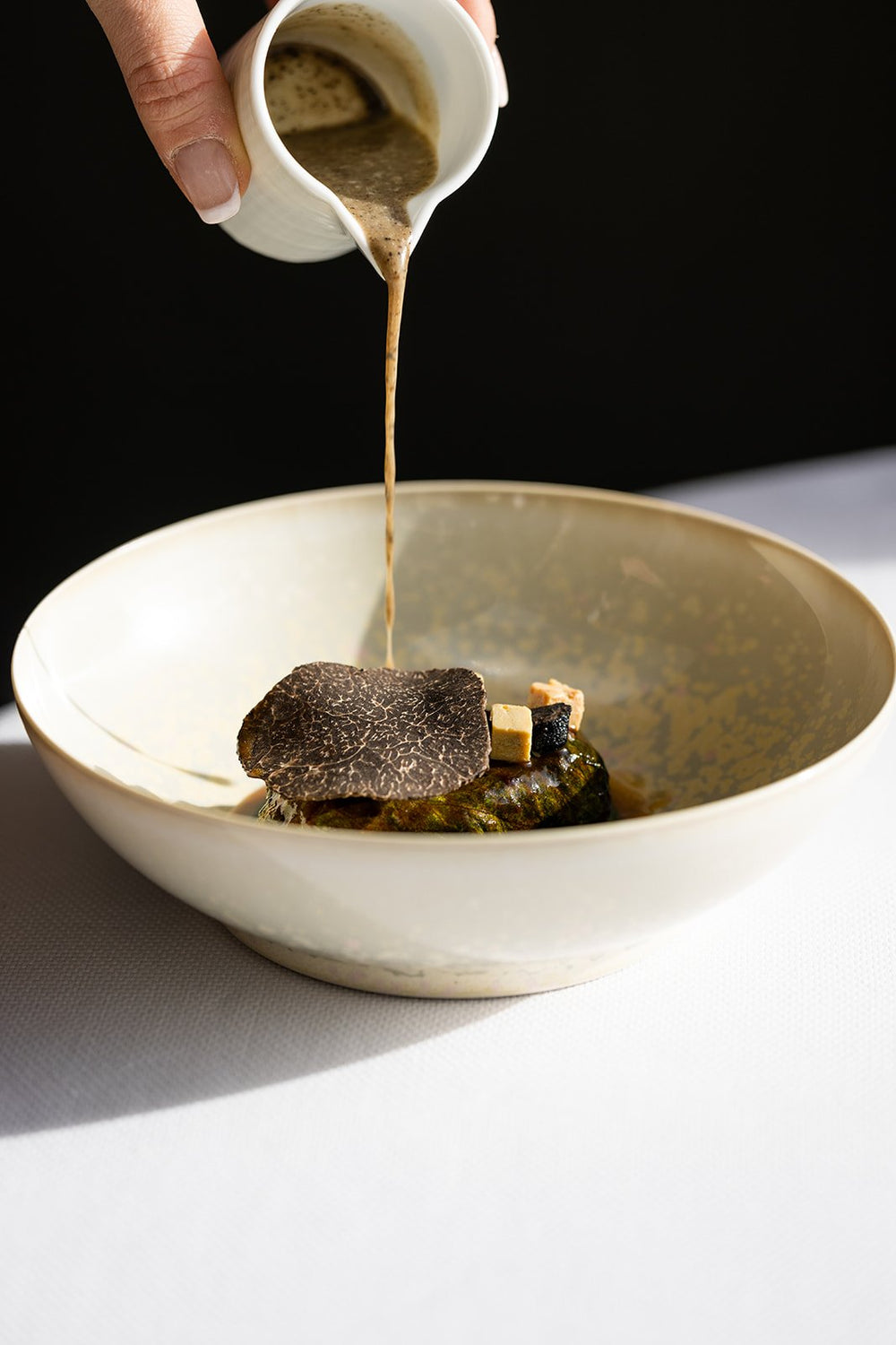 Sauce versée sur un plat gourmand avec truffe et garniture, dans une ambiance lumineuse.