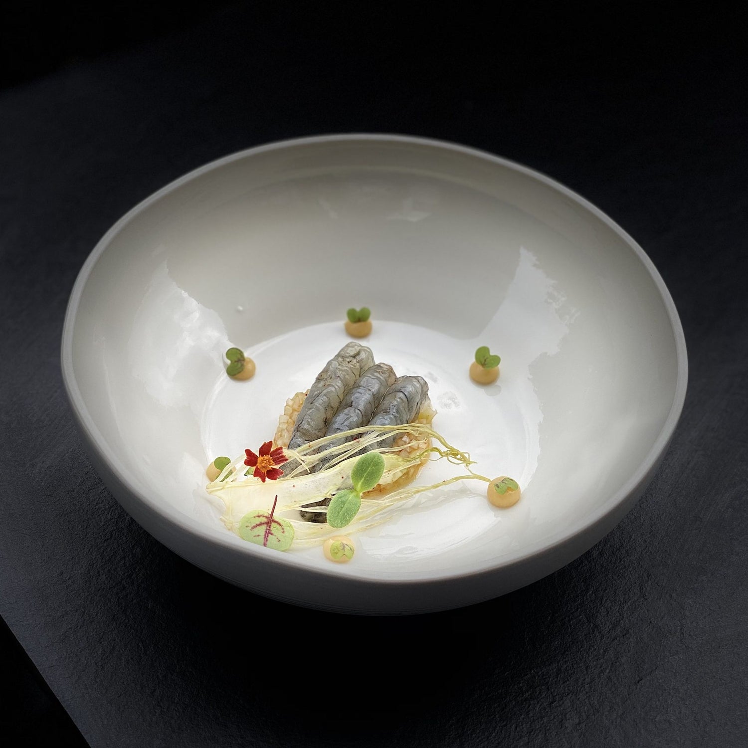 Plat gastronomique dans une assiette blanche avec des gambas et des éléments de décoration artistique.