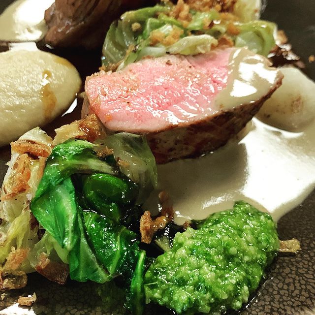 Filet d'agneau rosé servi avec des légumes verts sautés, une purée de brocoli, des gnocchis et une sauce crémeuse, le tout parsemé d'oignons croustillants.