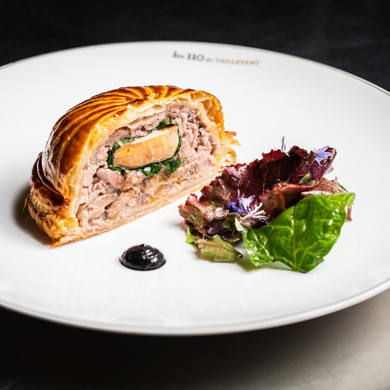 Pâté en croûte avec garniture de viande et légumes, accompagné de salade verte sur une assiette blanche.