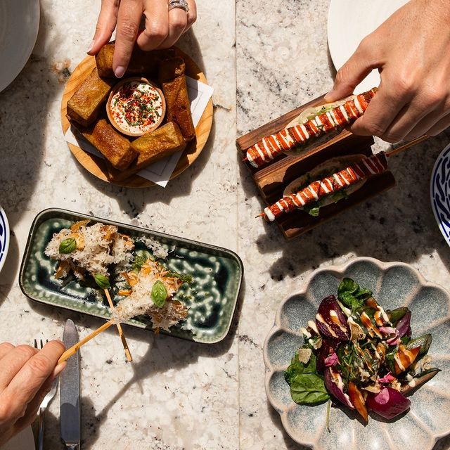 Une table de dîner avec une variété de plats, y compris des brochettes, une salade et des amuse-gueules, avec des mains atteignant la nourriture.
