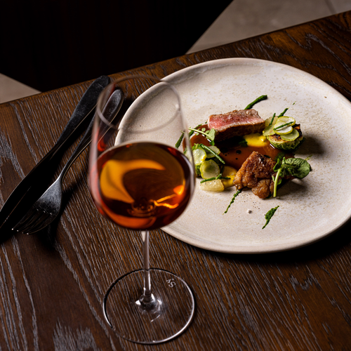 Plat raffiné avec viande et légumes verts, accompagné d’un verre de vin ambré
