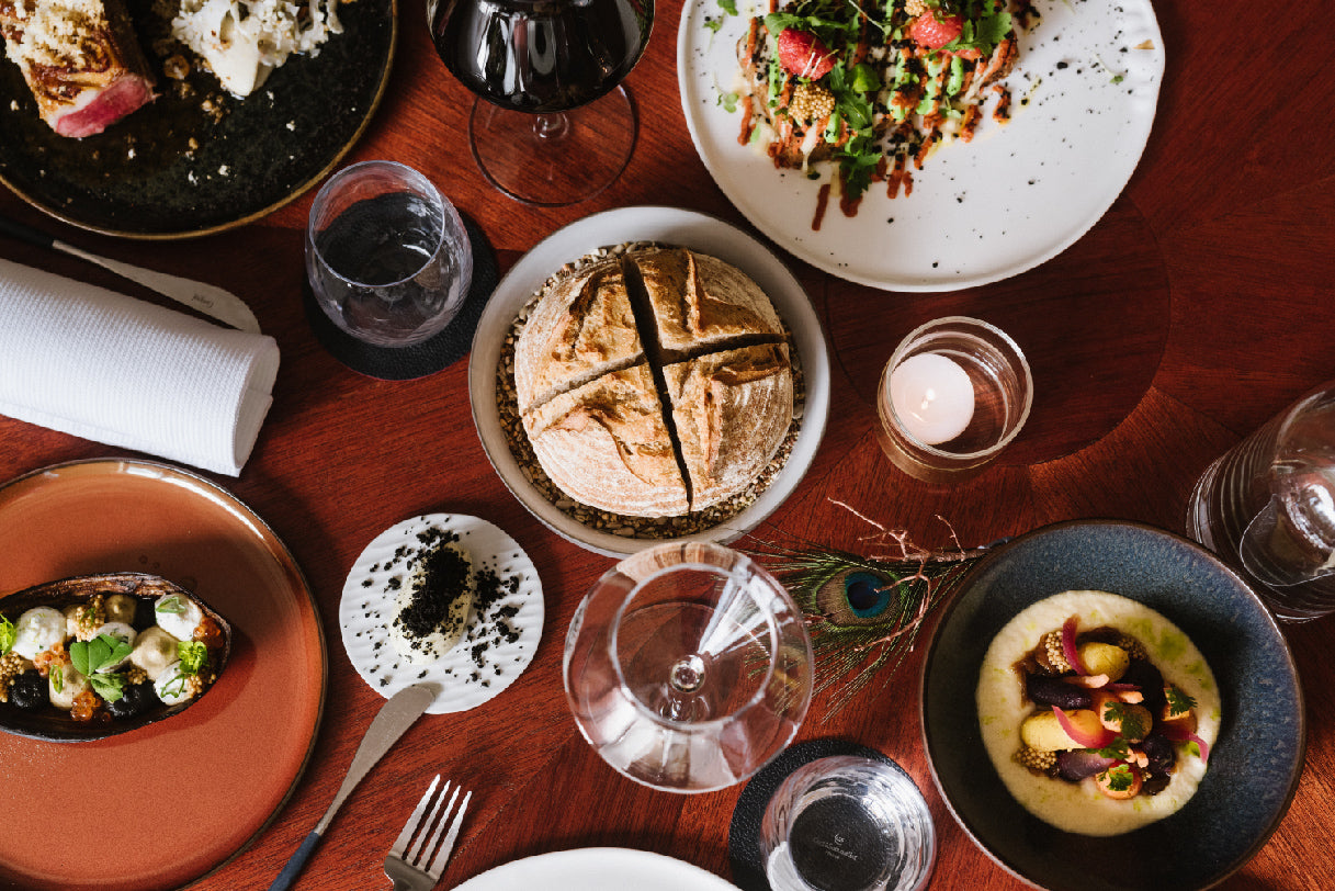 Table élégamment dressée avec une sélection de plats raffinés, comprenant du pain artisanal, des entrées créatives, et des accompagnements délicats, mis en valeur par une lumière douce et une ambiance chaleureuse.