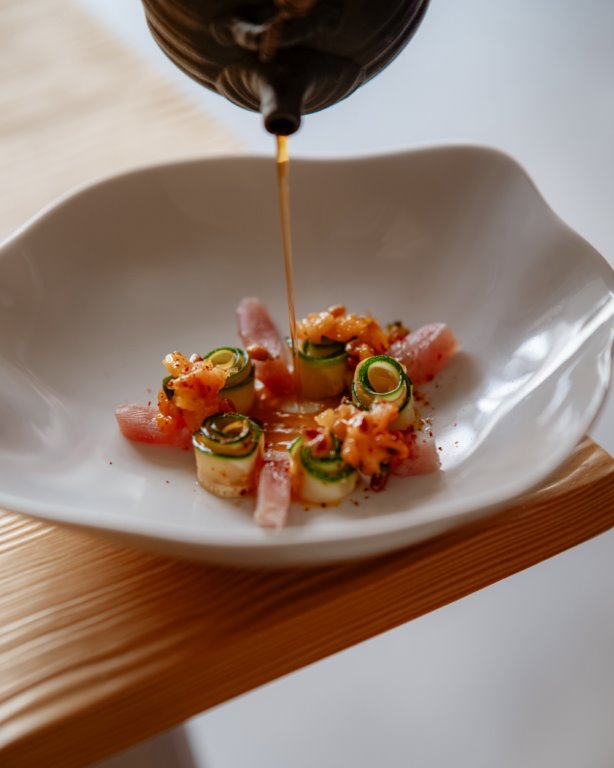 Chef versant une sauce sur un plat gourmet composé de légumes roulés et de poissons crus