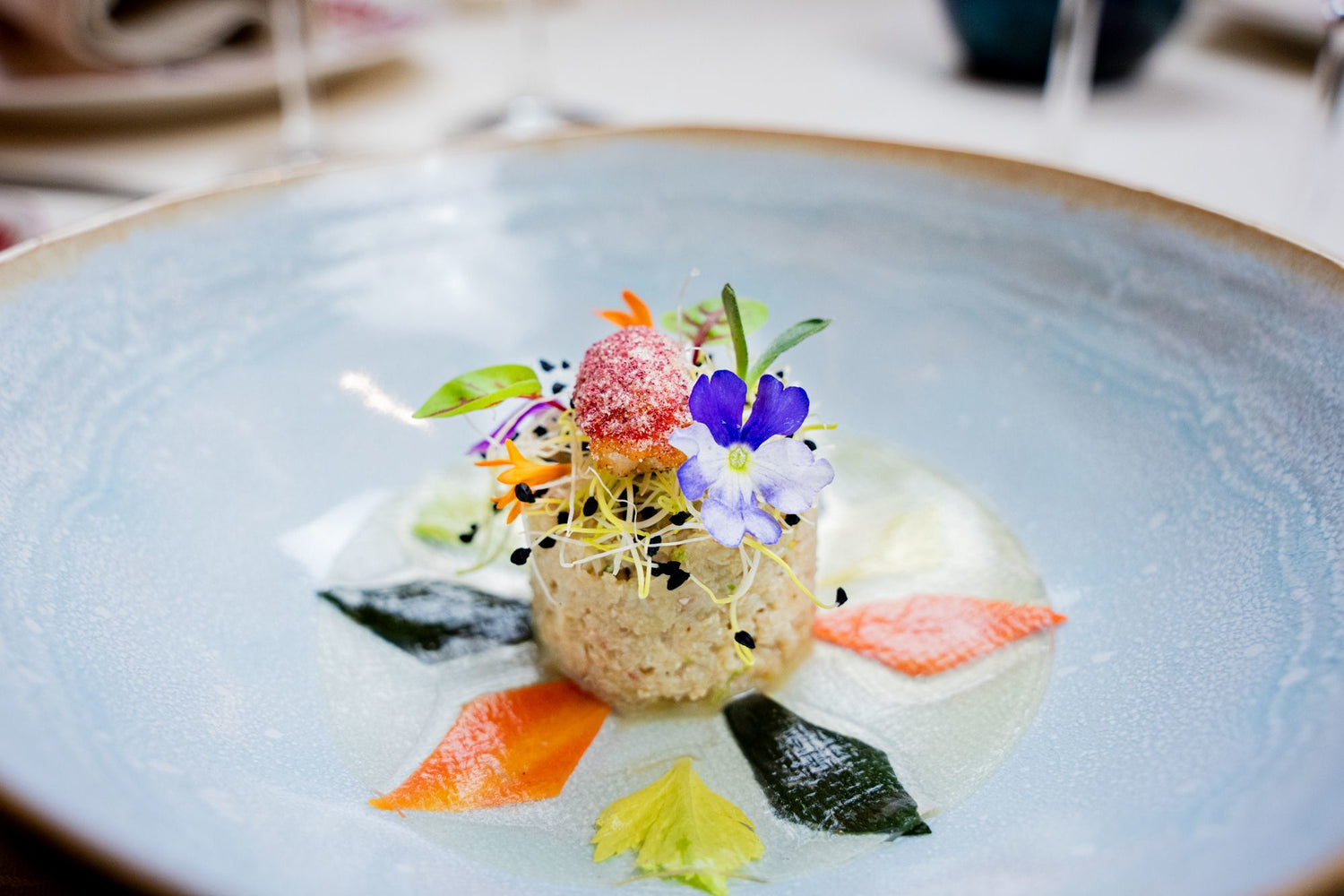 Plat gastronomique décoré avec des fleurs comestibles et des légumes colorés.