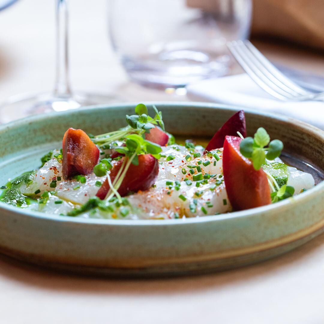 Plat de ceviche avec des morceaux de prunes et des herbes fraîches dans une assiette en céramique verte.
