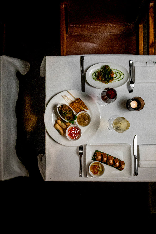 Vue aérienne d'une table dressée avec divers plats raffinés, comprenant des amuse-bouches, des entrées, un verre de vin rouge et un cocktail, créant une ambiance élégante et gastronomique.