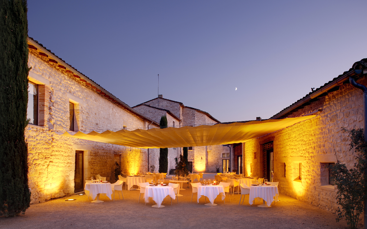 Cour extérieure d'un château, éclairée par une lumière douce au crépuscule, avec des tables dressées sous une grande toile tendue, créant une ambiance romantique.