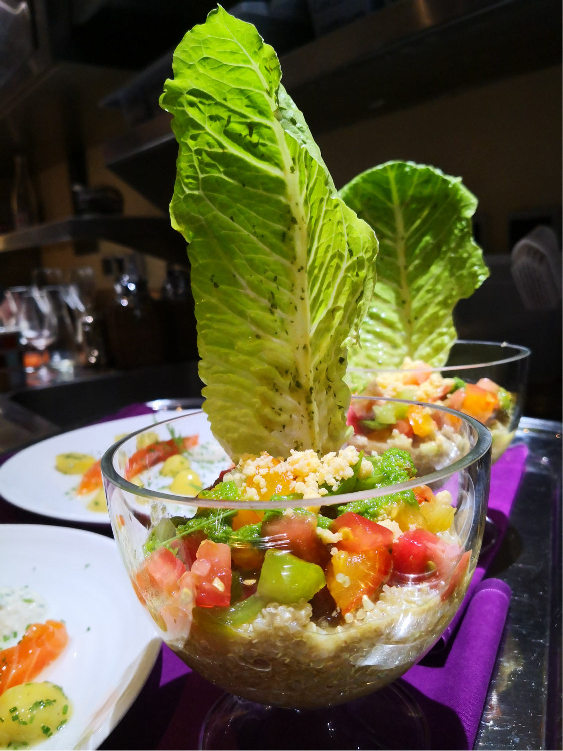 Salade de quinoa colorée servie dans une coupe en verre avec des feuilles de laitue romaine dressées verticalement.