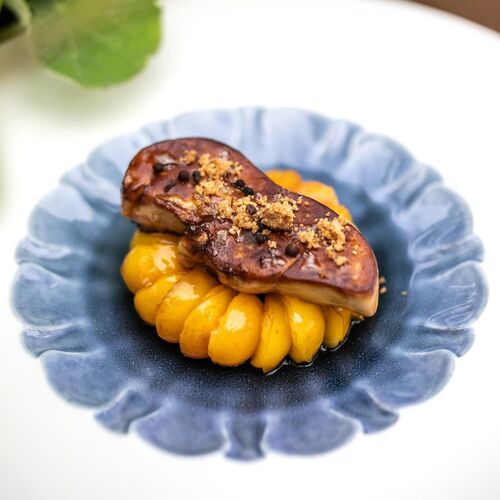 Foie gras poêlé servi sur une purée de légumes orange, présenté sur une assiette bleue.
