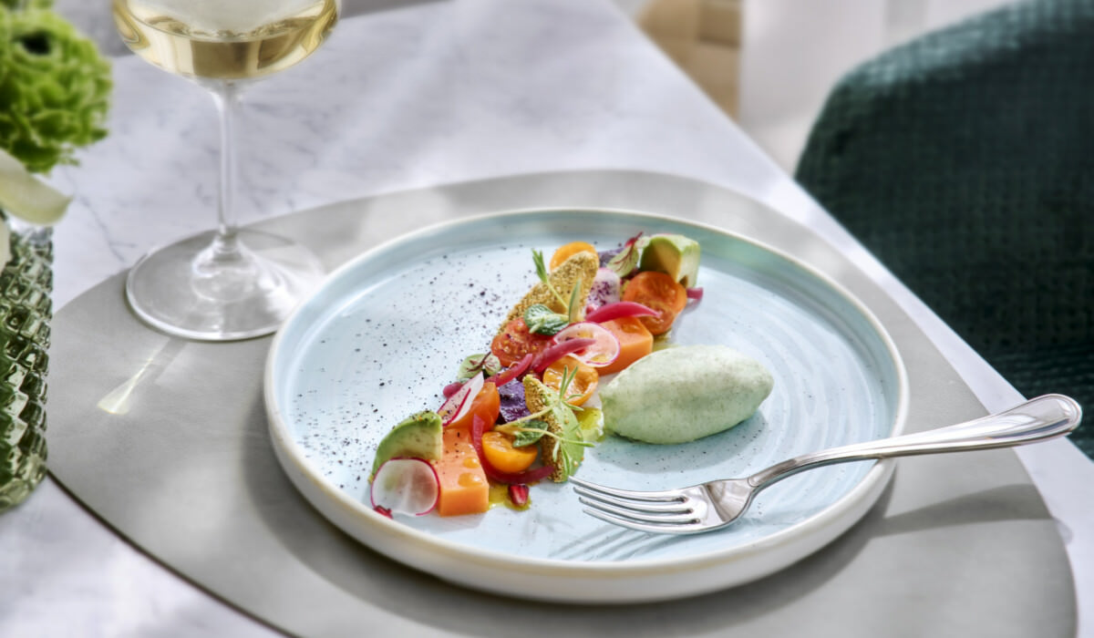Assiette colorée de légumes de saison avec une mousse légère aux herbes, accompagnée d'un verre de vin blanc.