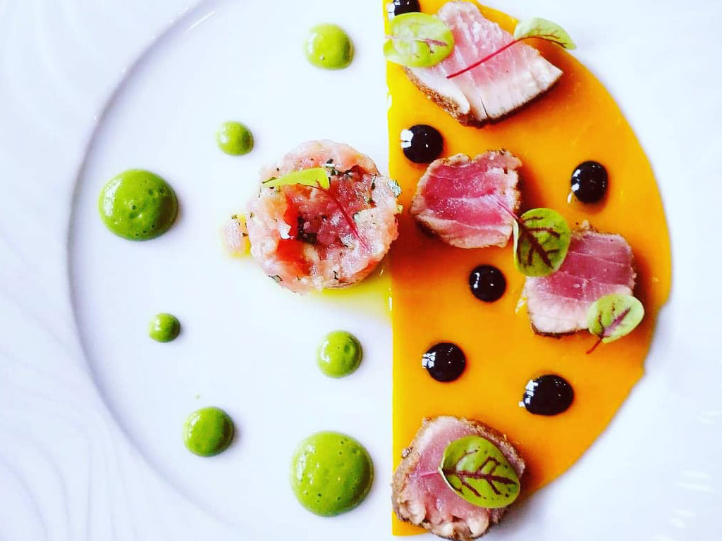 Présentation artistique d'un plat avec des morceaux de viande et des gouttes de sauce verte.