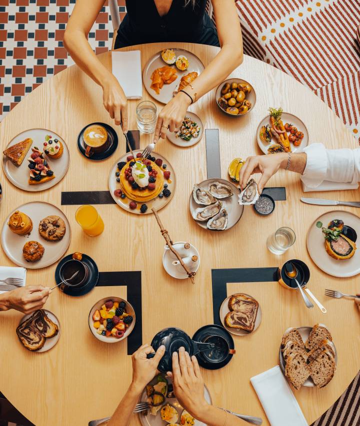 Jolie table dressée vue de haut avec plein de petits mets type brunch, huitre, pancakes, viennoiseries, fruits