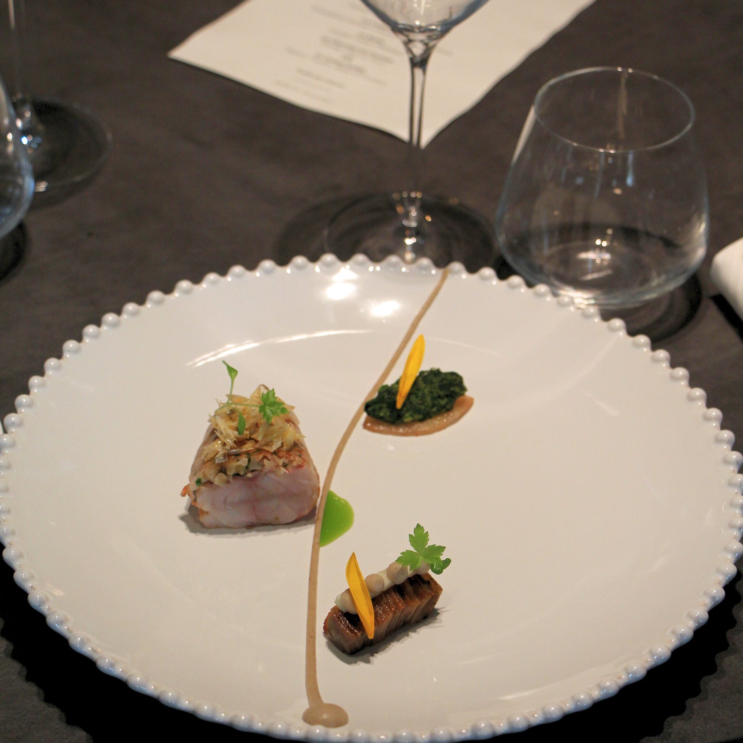 Assiette gastronomique minimaliste avec morceaux de viande, purées et herbes fines, dressée avec une grande précision.