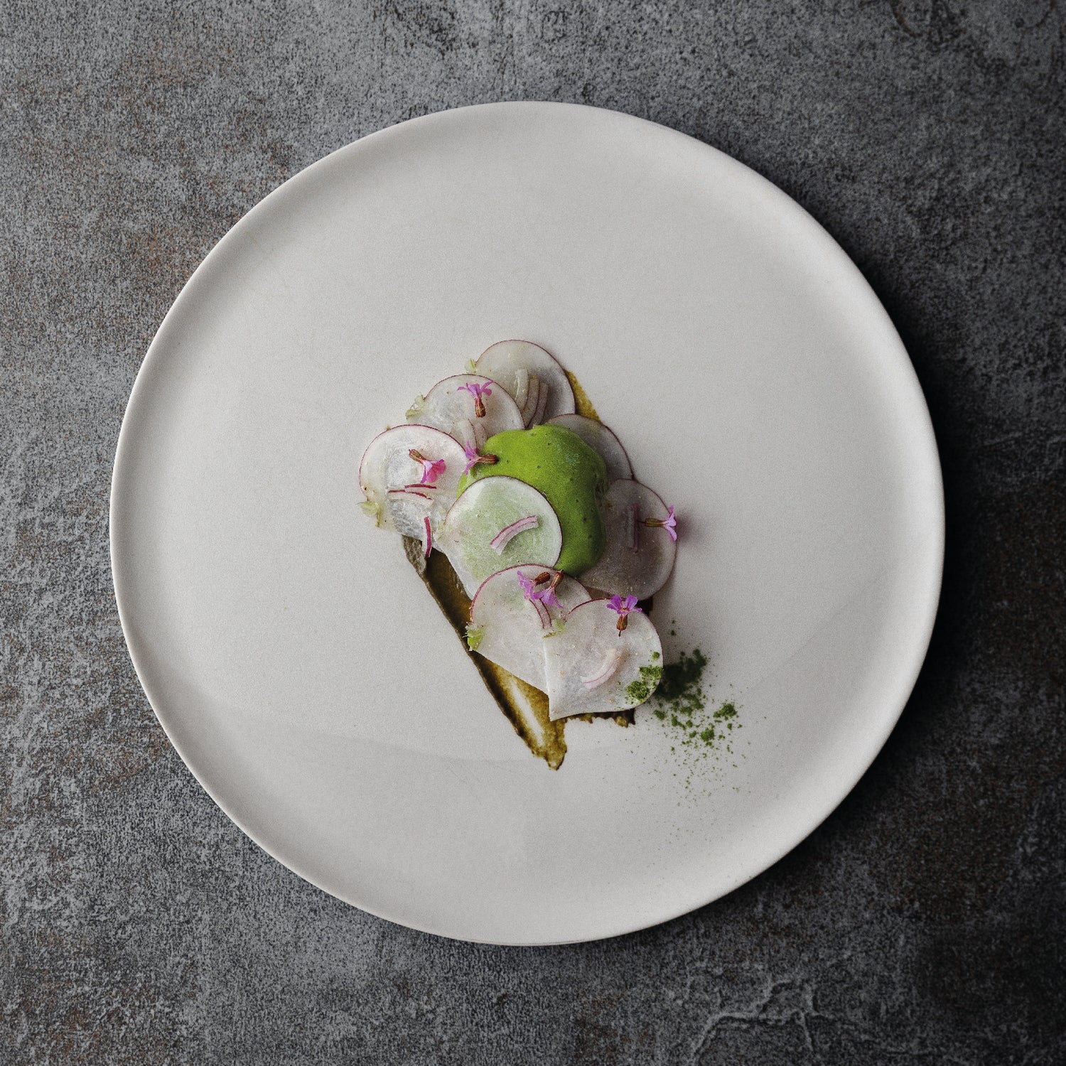 Assiette gastronomique élégante avec des tranches fines de radis et une quenelle verte, soigneusement disposées sur une assiette blanche minimaliste.