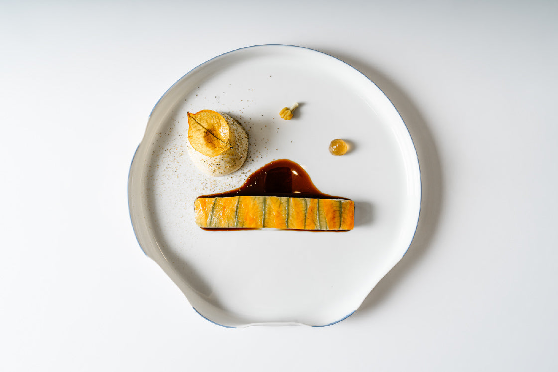 Présentation soignée d'un plat gastronomique avec un filet de poisson mariné, une sauce délicate et des accompagnements élégants, disposé sur une assiette blanche minimaliste.