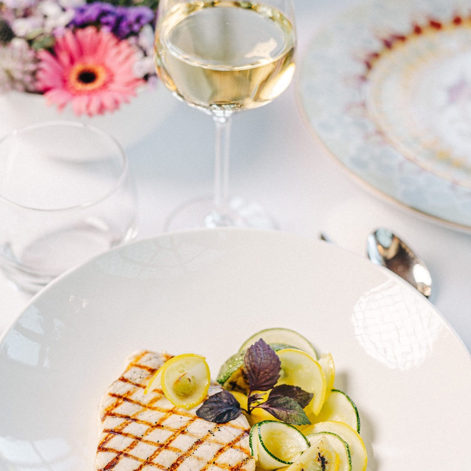 Jolie assiette de plat estival, poisson grillé au barbecue et courgettes roulées, verre de vin blanc devant l'assiette