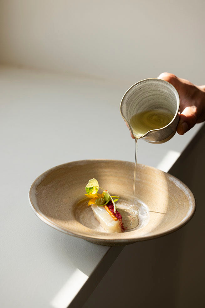 A hand pouring liquid over a plated dish with garnish.