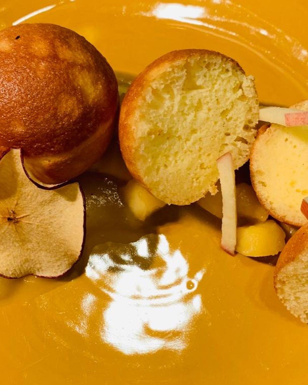 Gros plan sur un dessert composé de morceaux de gâteau moelleux, de tranches de pomme séchée et de garnitures délicates, présenté sur une assiette jaune brillante.