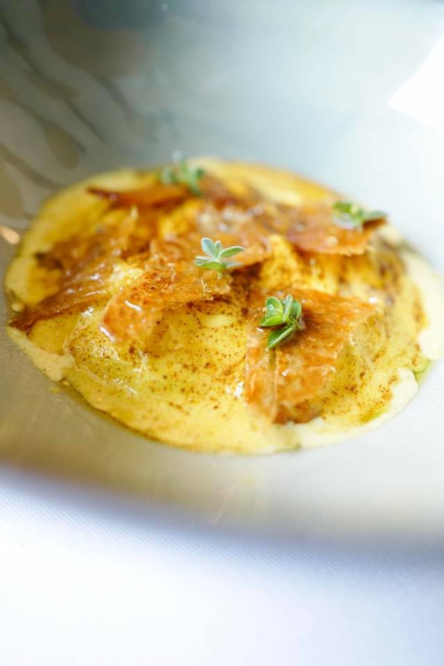 Plat de ravioles au fromage, garni de truffes et de jeunes pousses, servi dans une assiette creuse.