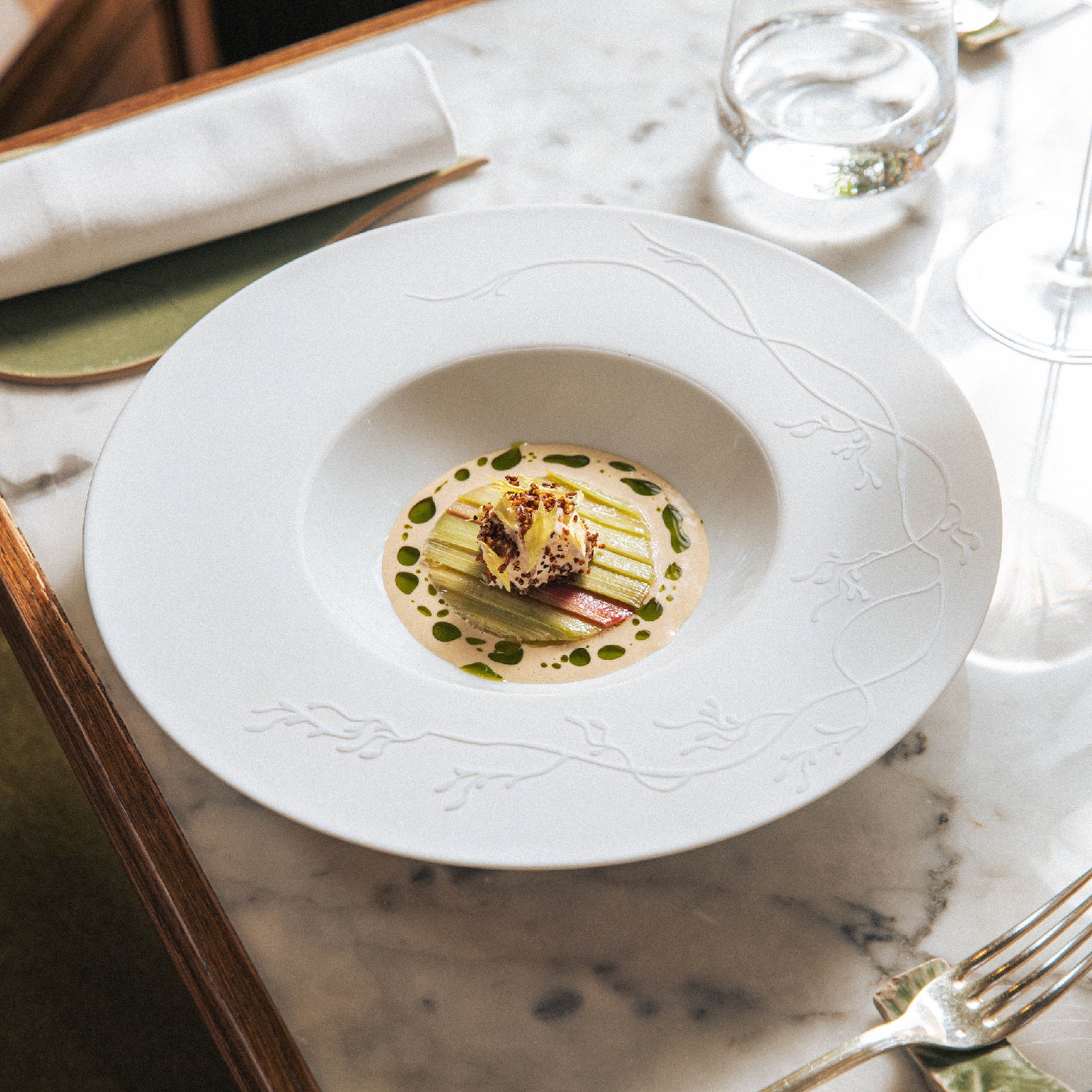 Assiette gastronomique élégante servie sur une table en marbre, composée de légumes finement dressés dans une sauce crémeuse parsemée de gouttes d’huile verte.