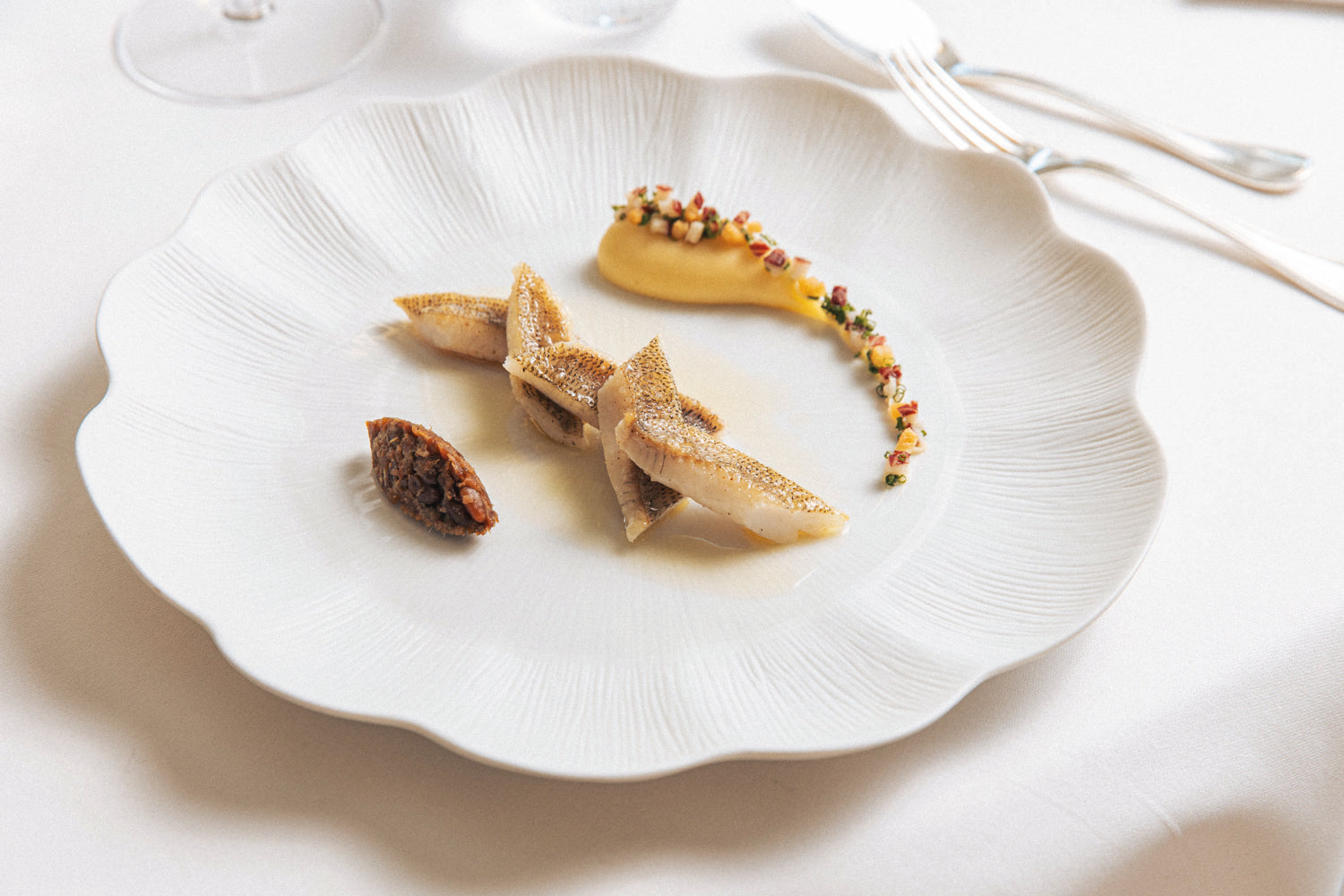 Assiette gastronomique élégante composée de filets de poisson, purée et garnitures colorées, servie sur une assiette blanche texturée.
